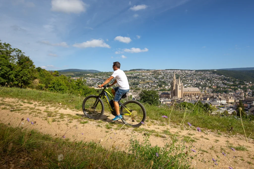A cyclist on the Causse de Mende, with a panoramic view of the town and Mende Cathedral.
